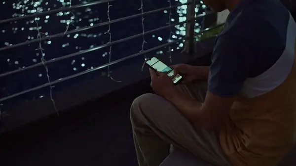 A person scrolling a phone on a balcony at night