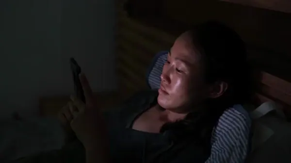 A woman lying in bed at night, lit by her phone
