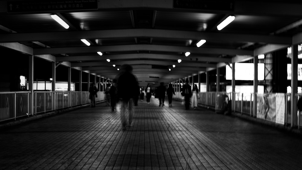 People walking through a long covered walkway, in black and white
