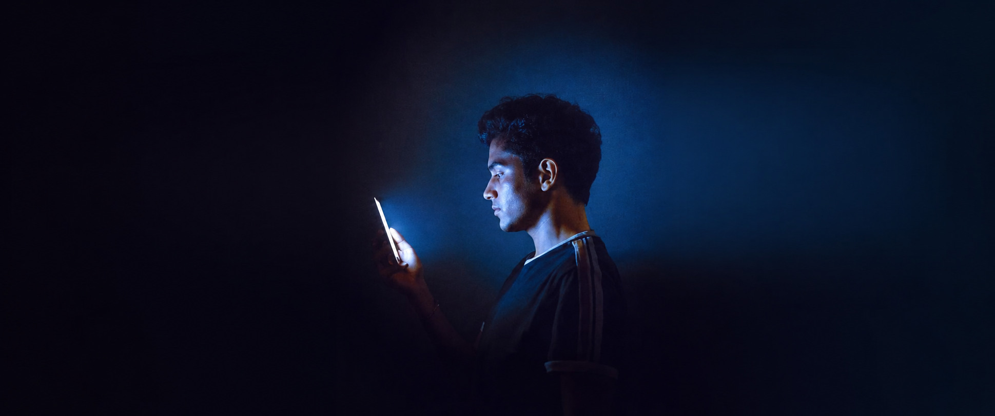 A man lit blue by his phone in the dark