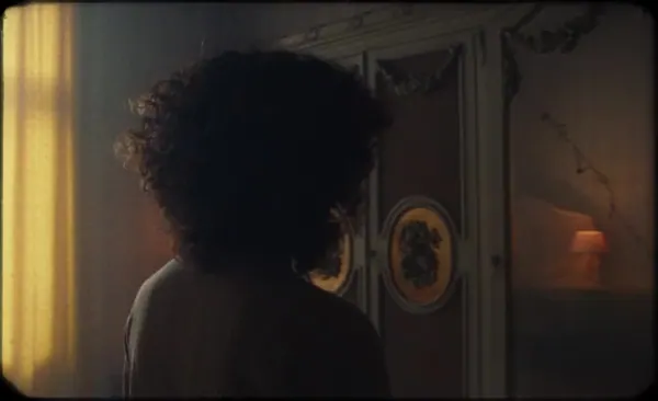 A person with curly hair seen from behind in a dim room